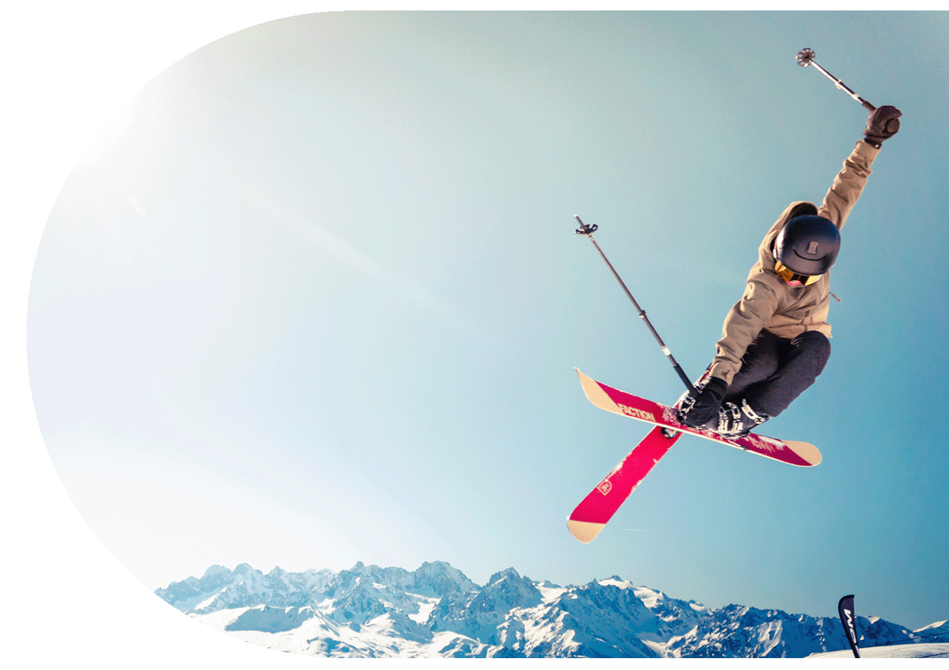Skier pictured in mid-air in front of snow capped mountains and a clear blue sky