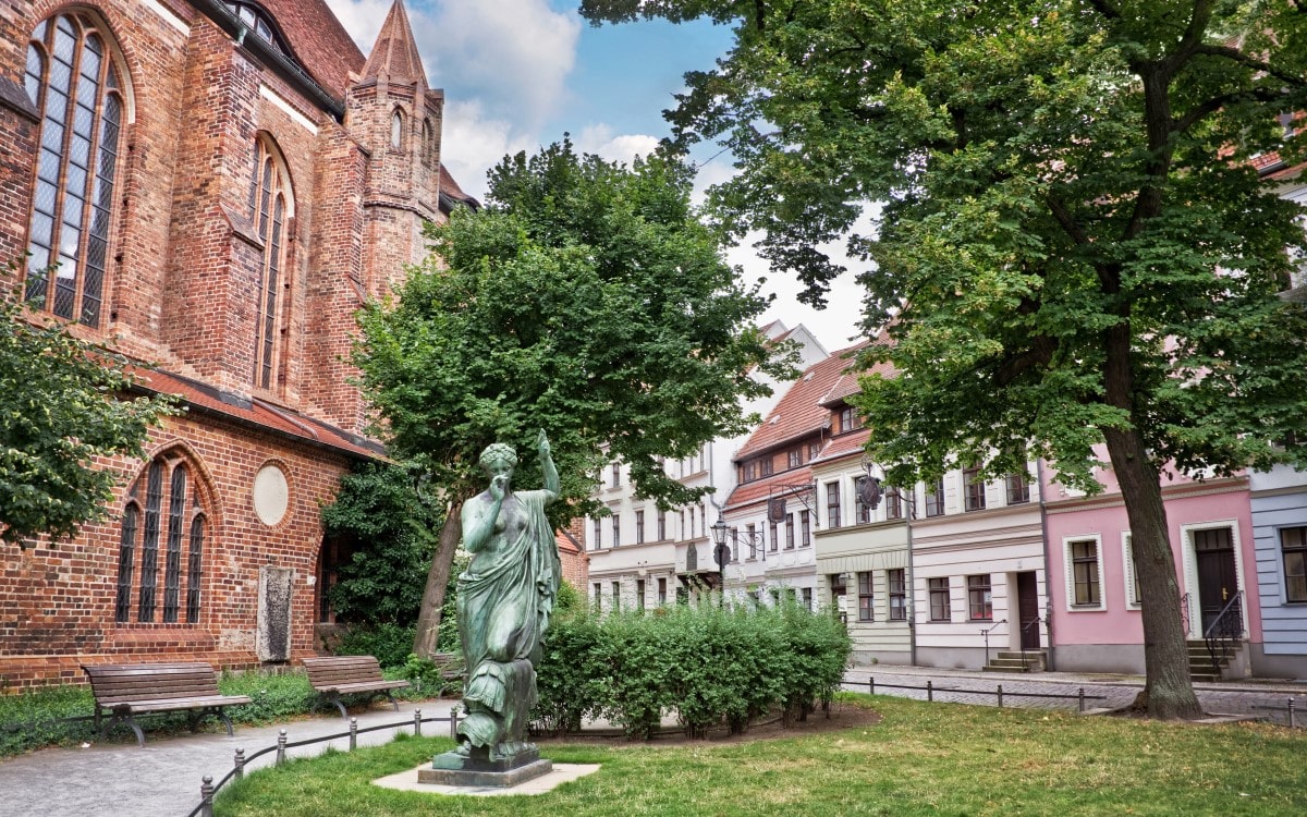 Old brick buildings and a statue nestled in a small green area, located in Nikolaivierte, Berlin