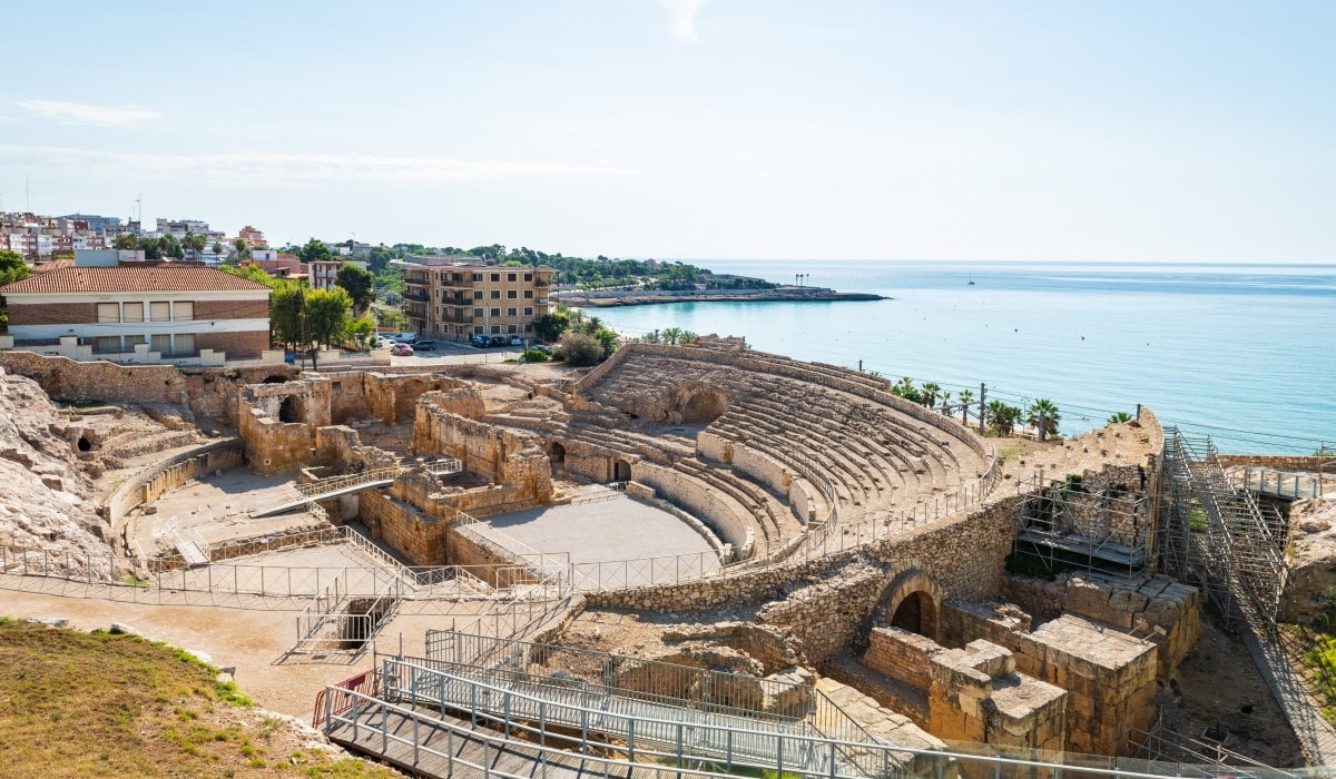 Wide-angle view of the ruins of the Roman amphitheatre in Tarragona, with the Mediterranean Sea in the background.